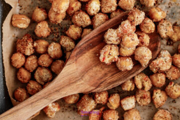 Close-up of roasted chickpeas coated in seasoning on parchment paper, with a wooden spoon scooping some up.