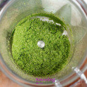 A top-down view of a food processor containing finely ground Basil Salt powder on a wooden surface.