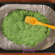 A yellow spatula rests on a baking tray lined with parchment paper, holding a spread-out layer of Basil Salt