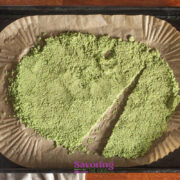 Basil Salt baked spread on a round parchment-lined baking sheet, with a diagonal section cut out, on a wooden surface.