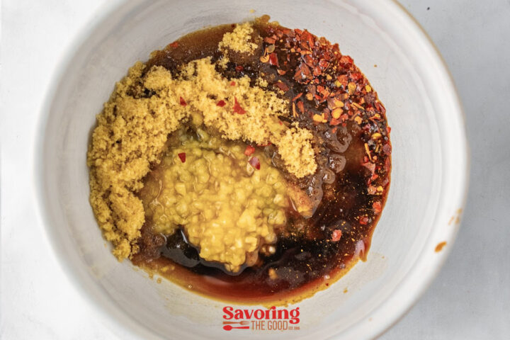 A white bowl containing brown sugar, minced garlic, soy sauce, red pepper flakes, and other liquid seasonings, seen from above for the sauce of Beef lo mein.