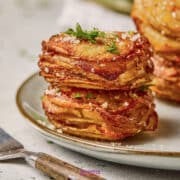 Two delicious potato stacks of thinly sliced, baked potatoes are garnished with chopped herbs and grated cheese on a ceramic plate.