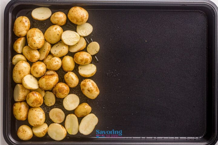 A baking tray with halved and whole seasoned baby potatoes spread on one side, ready for roasting alongside sheet pan salmon.