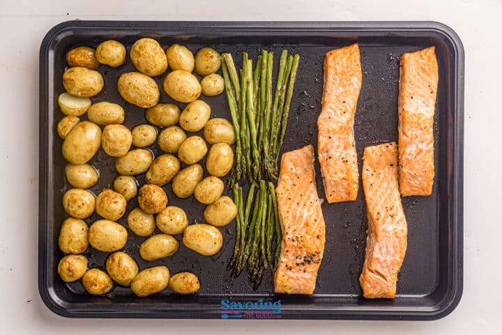 Sheet pan salmon paired with roasted baby potatoes and asparagus spears, all seasoned and arranged neatly on a black baking tray.