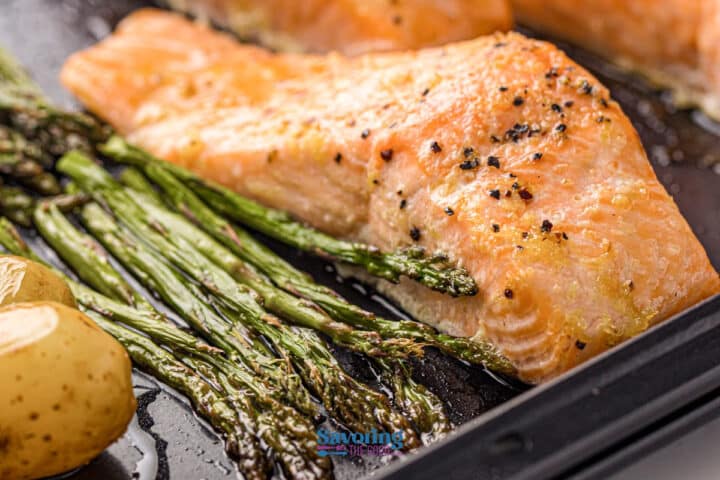 Sheet pan salmon fillet baked with black pepper, roasted asparagus spears, and halved baby potatoes, all on a single baking sheet.