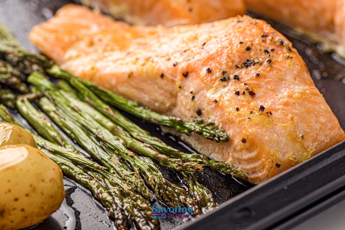 Sheet pan salmon fillet baked with black pepper, roasted asparagus spears, and halved baby potatoes, all on a single baking sheet.