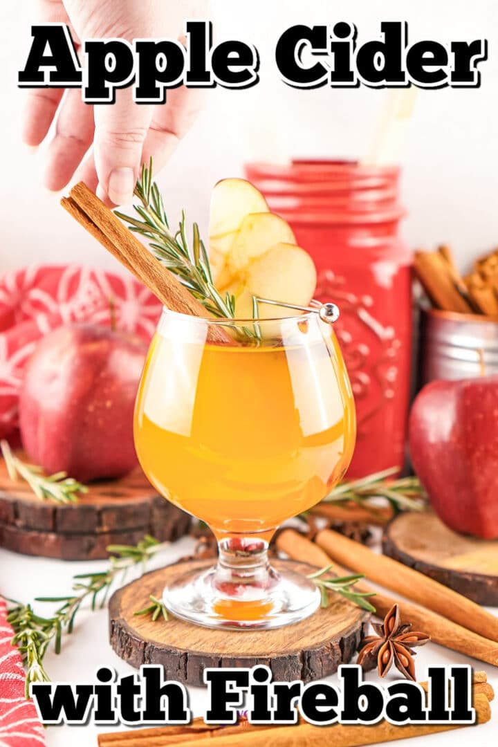 A hand places a cinnamon stick and rosemary garnish in a glass of apple cider, with apples and cinnamon sticks in the background. Text reads: "Apple Cider with Fireball.