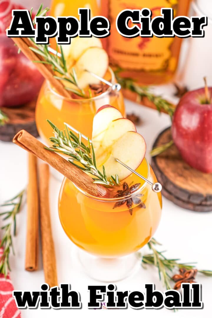Two glasses of apple cider with Fireball, garnished with apple slices, rosemary, cinnamon sticks, and star anise, surrounded by apples and cinnamon sticks.