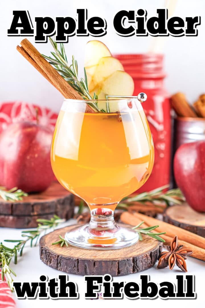 A glass of apple cider garnished with apple slices, a cinnamon stick, and rosemary, surrounded by apples, cinnamon sticks, and a red container in the background. Text reads "Apple Cider with Fireball.