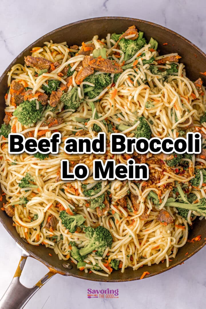 A skillet filled with beef and broccoli lo mein noodles, topped with pieces of broccoli and shredded carrots.