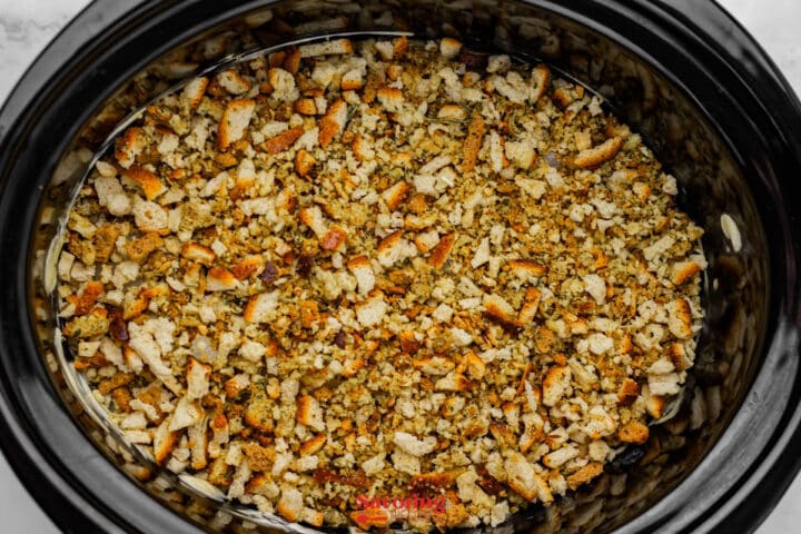 A slow cooker filled with seasoned bread cubes and stuffing mix, ready to be cooked.