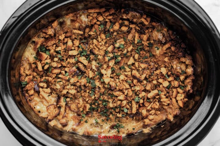 A slow cooker filled with a baked casserole topped with a golden-brown layer of crushed crackers and sprinkled herbs.