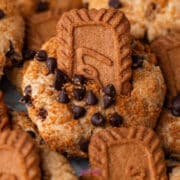 A close-up of cookies topped with chocolate chips, cookie crumbs, and a rectangular biscoff butter cookie partially inserted into each cookie.