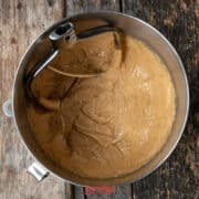 A mixing bowl with biscoff butter cookie batter and a metal beater attachment sits on a rustic wooden surface.