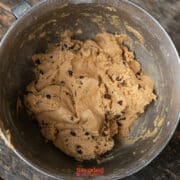A metal mixing bowl filled with biscoff butter cookie dough sits on a rustic wooden table.