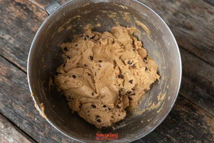 A metal mixing bowl filled with biscoff butter cookie dough sits on a rustic wooden table.