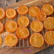 Slices of candied orange laid out in rows on a wire cooling rack placed over a wooden cutting board.
