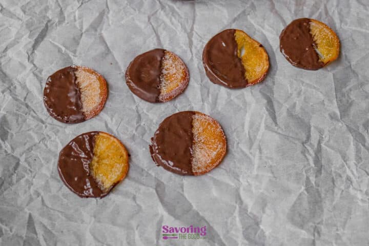 Six candied orange slices partially dipped in chocolate are arranged on crumpled parchment paper.
