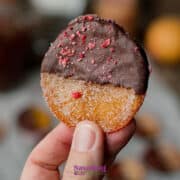 A hand holds a candied orange slice half-dipped in chocolate, sprinkled with pink crumbs .