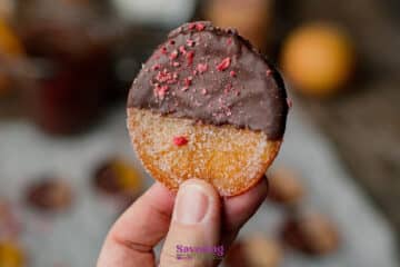 A hand holds a candied orange slice half-dipped in chocolate, sprinkled with pink crumbs .