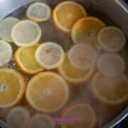 Sliced oranges and lemons simmer in a large pot of water on a stovetop.
