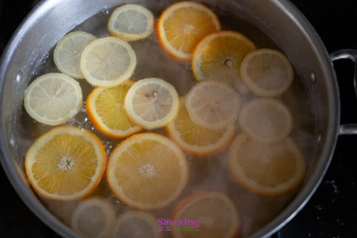 Sliced oranges and lemons simmer in a large pot of water on a stovetop.