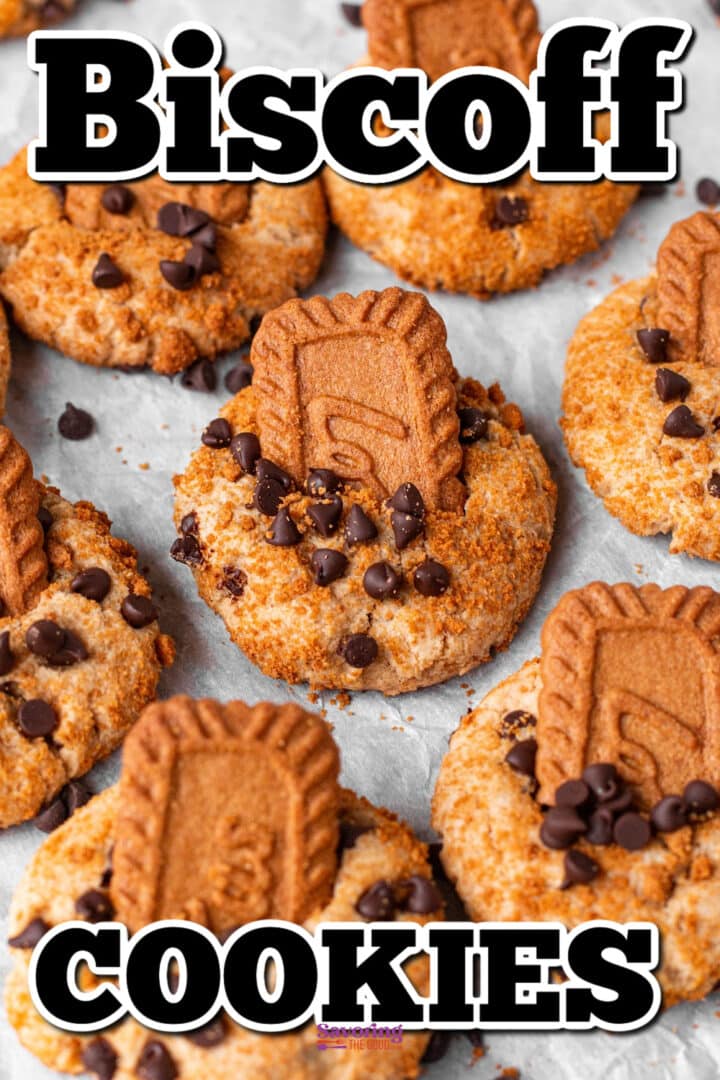 Several cookies topped with Biscoff biscuits and chocolate chips arranged on a sheet of parchment paper.