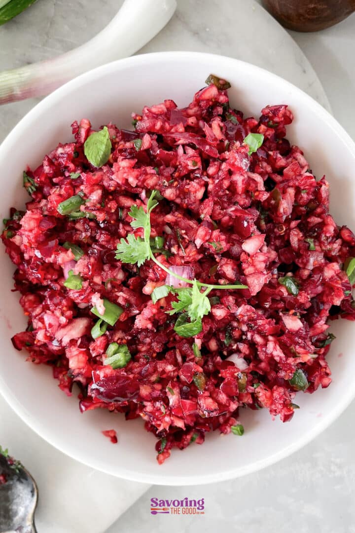 A white bowl filled with finely chopped beet salsa, garnished with cilantro, placed on a marble surface.