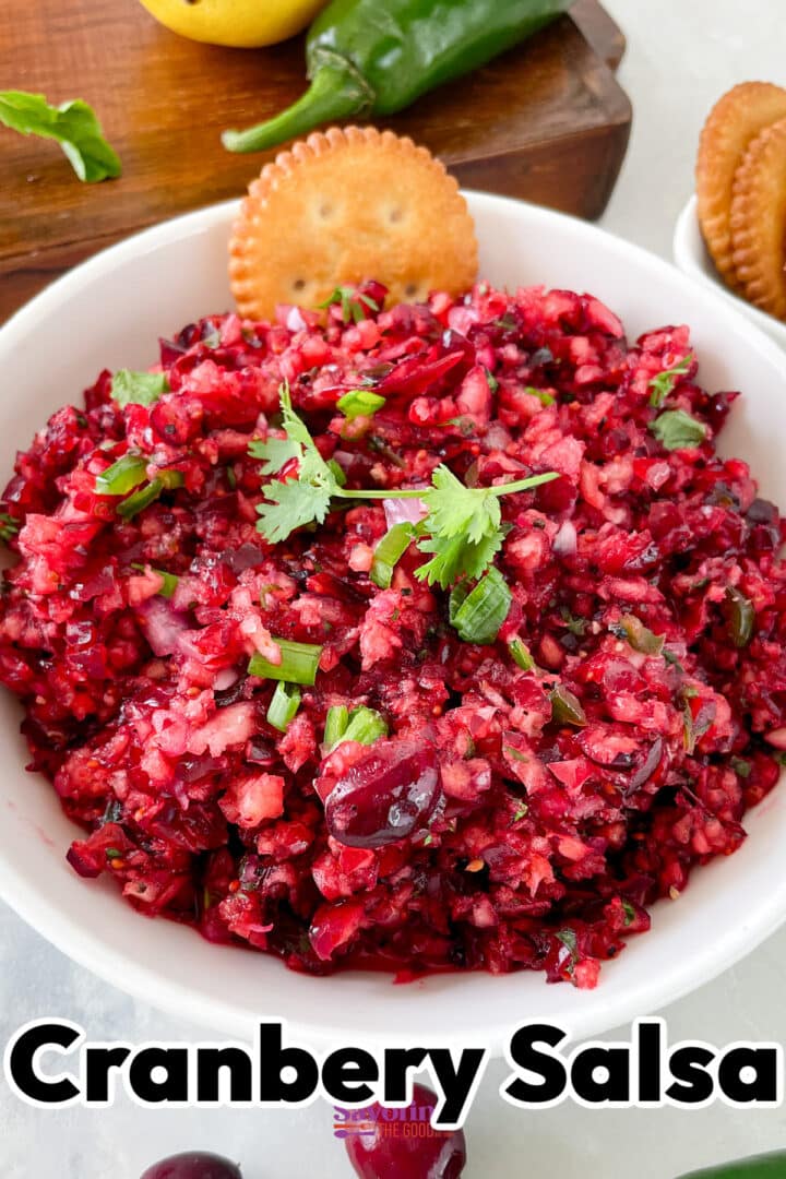 A white bowl filled with cranberry salsa garnished with cilantro, next to round crackers. The text "Cranberry Salsa" is at the bottom of the image.