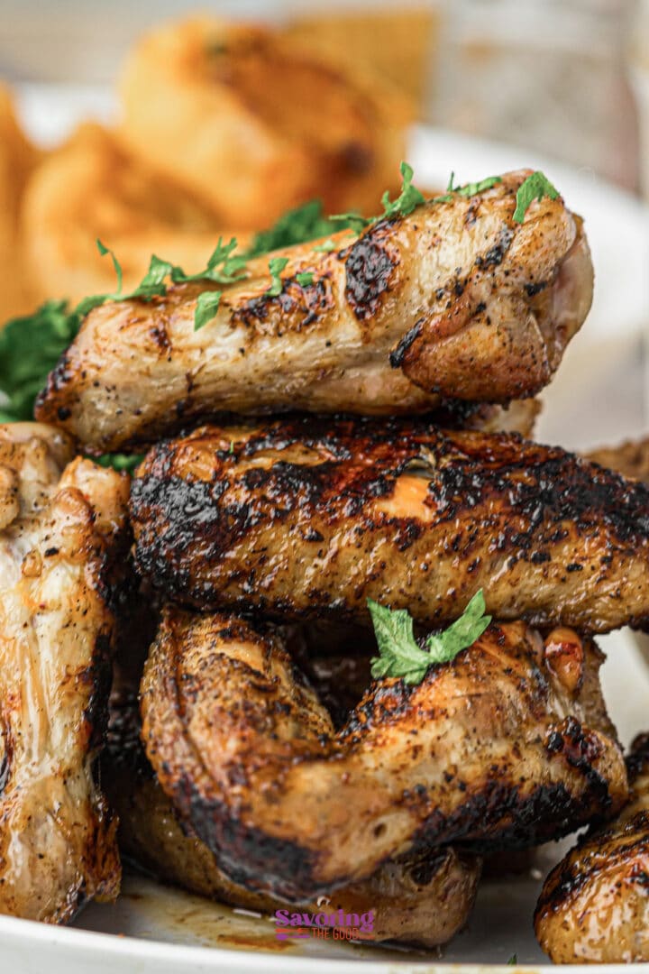 A close-up of grilled chicken wings garnished with chopped herbs, served on a white plate.