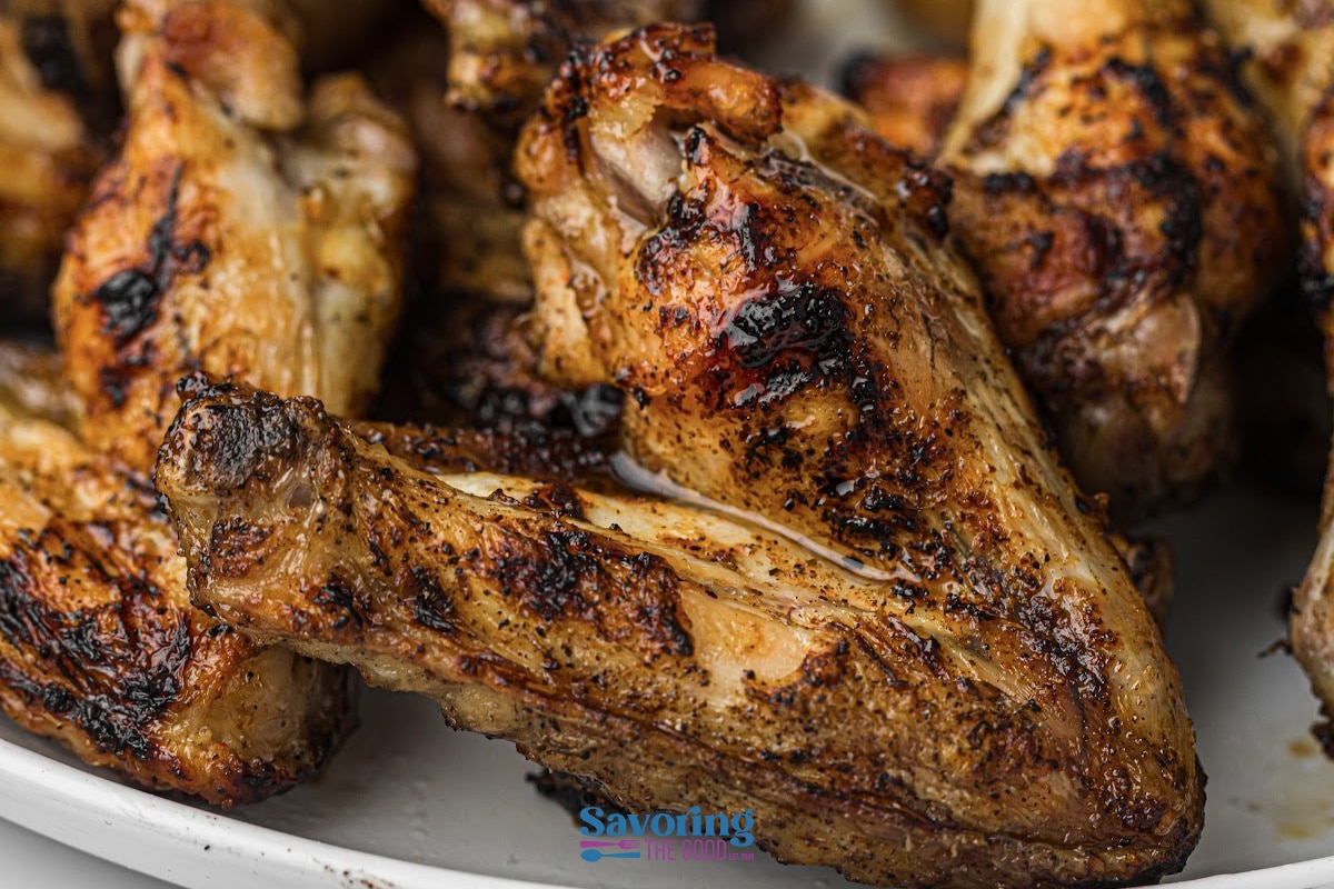 Close-up of several grilled chicken wings on a white plate, showing charred and seasoned skin.