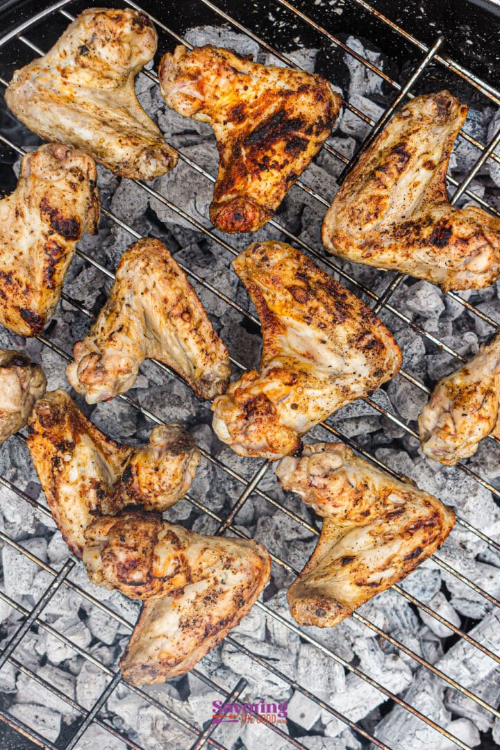 Chicken wings are grilling on a metal rack over hot charcoal, showing visible grill marks and a smoky, charred appearance.