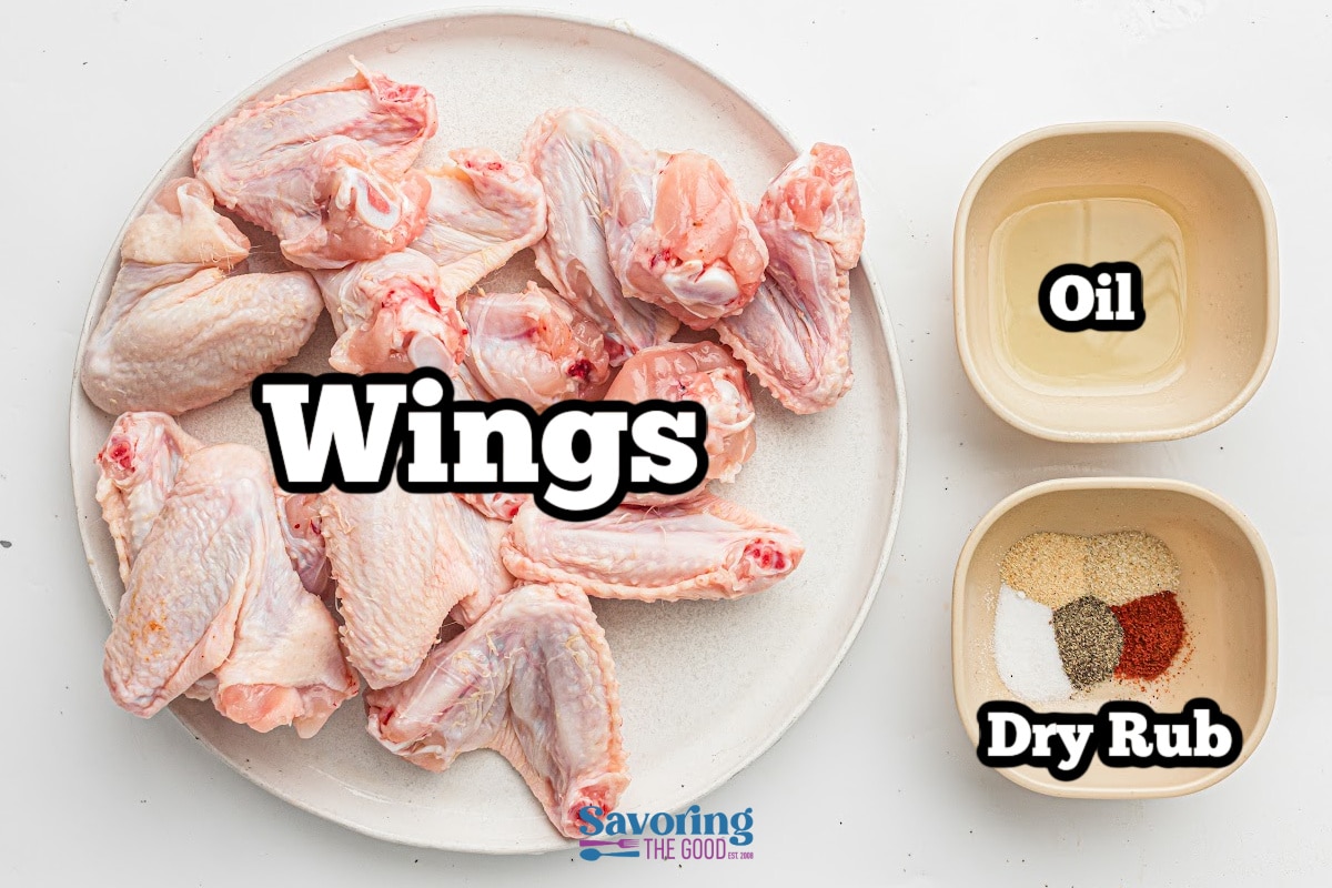 A plate of raw chicken wings next to two bowls, one with oil and one with assorted dry spices labeled "Dry Rub.
