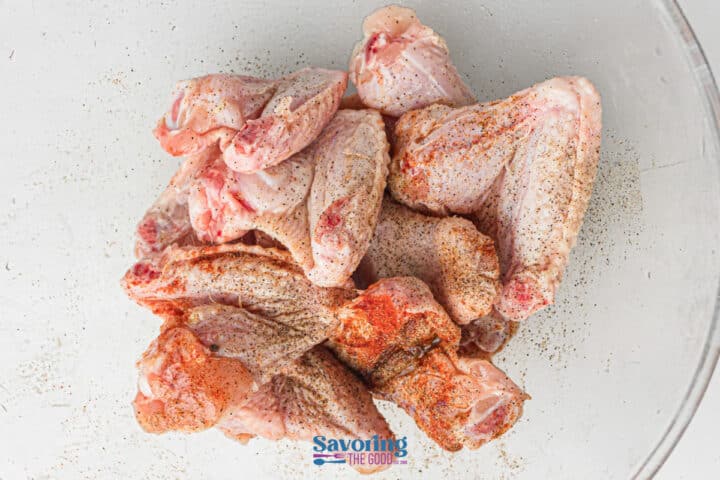 Raw chicken wings coated in a flavorful dry rub are placed in a clear glass bowl, ready to be transformed into delicious grilled chicken wings.