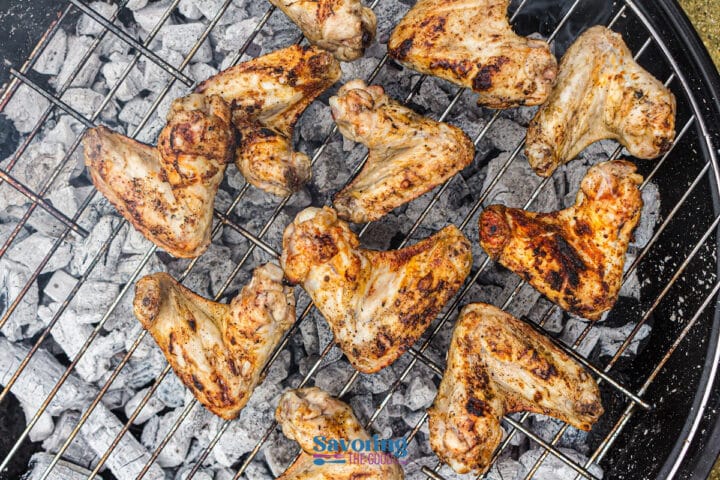 Grilled chicken wings coated in a flavorful dry rub sizzle on a metal grate over hot charcoal, with char marks and smoke rising.