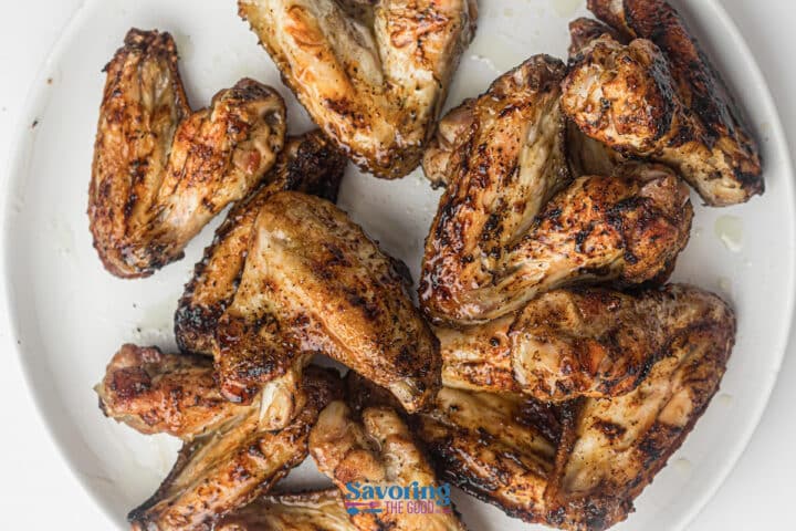 A white plate filled with several grilled chicken wings, seasoned and cooked with visible grill marks.
