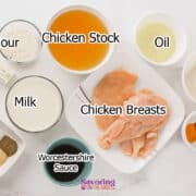 Ingredients for a recipe laid out in bowls and plates, including chicken breasts, flour, chicken stock, oil, butter, milk, Worcestershire sauce, and spices on a white surface.