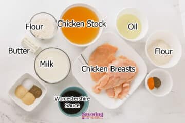 Ingredients for a recipe laid out in bowls and plates, including chicken breasts, flour, chicken stock, oil, butter, milk, Worcestershire sauce, and spices on a white surface.