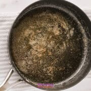 A black saucepan with browned butter residue sits on a white textured cloth on a marble surface.