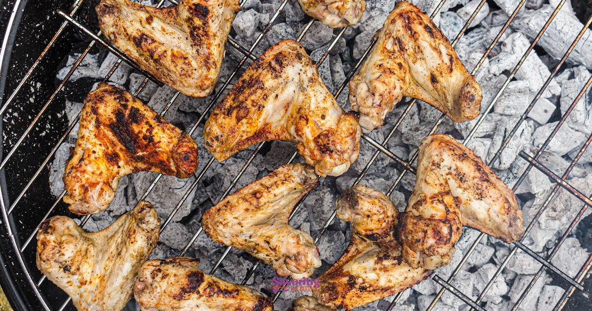 Chicken wings grilling on a metal grate over hot charcoal, showing grill marks and seasoning on the wings.
