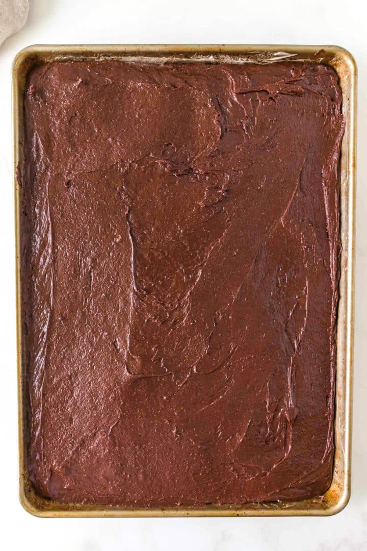 A baking sheet filled with an even layer of unbaked chocolate cake batter on a white surface.