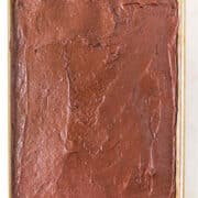 A rectangular sheet cake covered with smooth chocolate frosting on a baking tray.