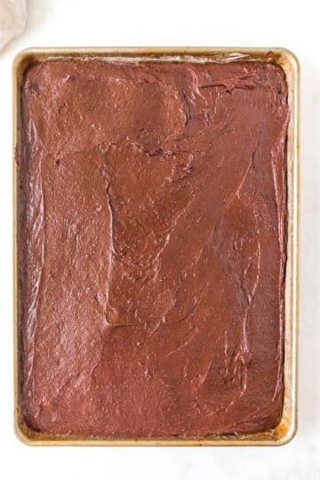 A rectangular sheet cake covered with smooth chocolate frosting on a baking tray.