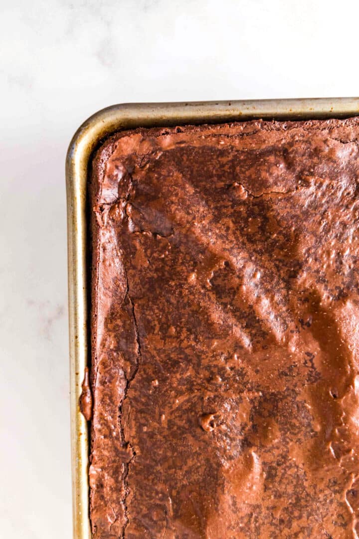 A close-up of a metal baking pan filled with freshly baked Sheet Pan Brownies, showing a cracked, glossy surface.