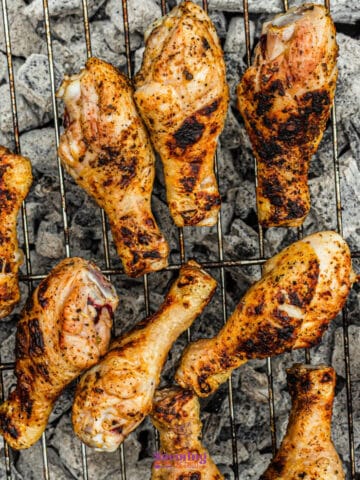 Grilled chicken drumsticks with char marks on a metal grate over hot coals.