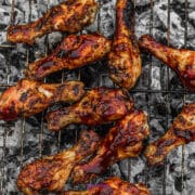 Grilled chicken drumsticks with barbecue sauce cooking on a metal grate over hot charcoal.