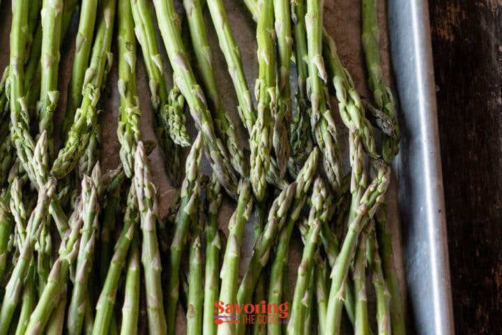 A baking tray filled with raw asparagus spears arranged in a single layer on parchment paper.