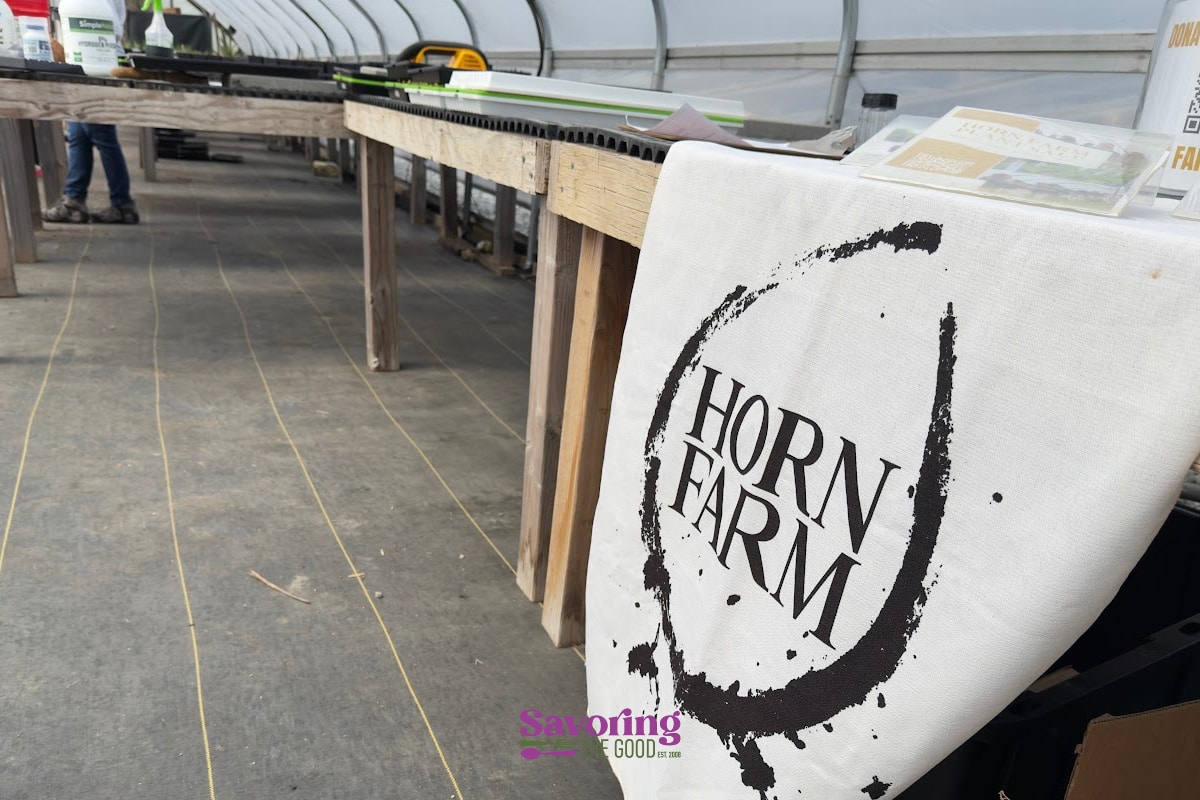 A banner reading "Horn Farm" hangs from a table in a greenhouse, with supplies and growing trays visible on the tables.