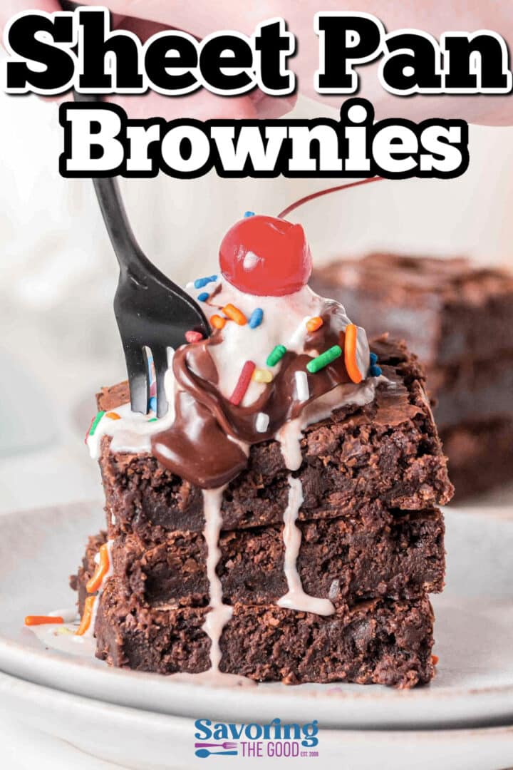 A stack of brownies topped with whipped cream, chocolate syrup, sprinkles, and a cherry, with a black fork inserted, on a white plate.