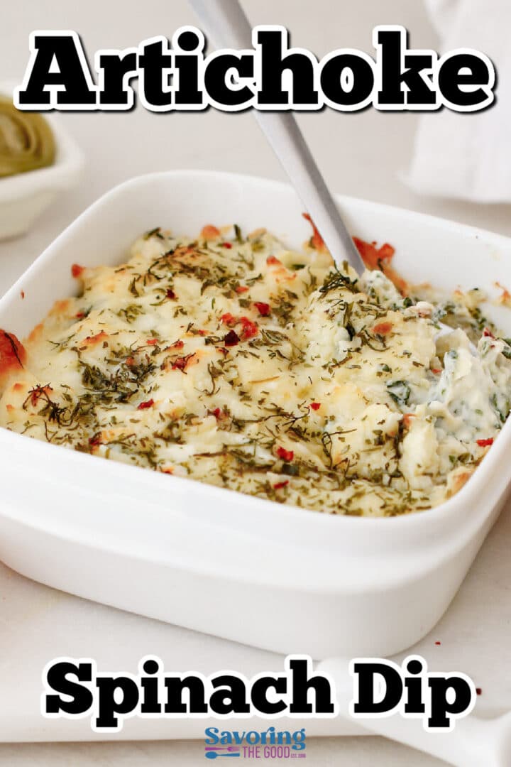 A white square dish filled with baked artichoke spinach dip, topped with melted cheese and herbs, with a spoon inside.